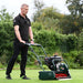 Man operating the Allett Kensington 20H petrol cylinder mower on a lush green lawn, demonstrating its precision cutting and smooth self-propelled operation.