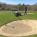 Groundskeeper using a Martin Lishman Micro-Spray turf sprayer on a golf course near a sand bunker. The sprayer applies precise treatments for turf health and weed control, ensuring consistent coverage and professional maintenance of fairways, greens, and surrounding landscaped areas.