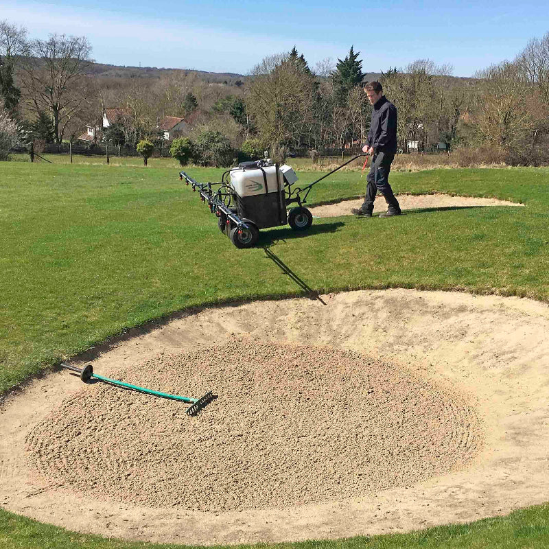 Groundskeeper using a Martin Lishman Micro-Spray turf sprayer on a golf course near a sand bunker. The sprayer applies precise treatments for turf health and weed control, ensuring consistent coverage and professional maintenance of fairways, greens, and surrounding landscaped areas.