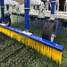 Close-up view of the Campey UniRake showing its yellow brush attachment, supporting wheels, and spring tines working on synthetic turf. The UniRake maintains artificial pitches by brushing infill evenly, lifting fibers, and enhancing play quality, durability, and drainage efficiency.