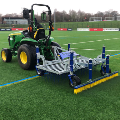 Campey UniRake attached to a John Deere tractor shown in action on an artificial sports pitch. The UniRake features spring tines and a rear brush, maintaining synthetic turf by lifting pile, removing debris, and evenly distributing infill across the surface.