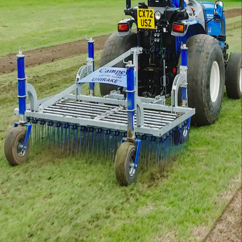 Rear field operation view of the Campey UniRake attached to a blue tractor with wide turf tyres. The UniRake’s flexible spring tines are working the grass surface to relieve compaction, improve aeration, and maintain healthy natural sports turf and pitches.