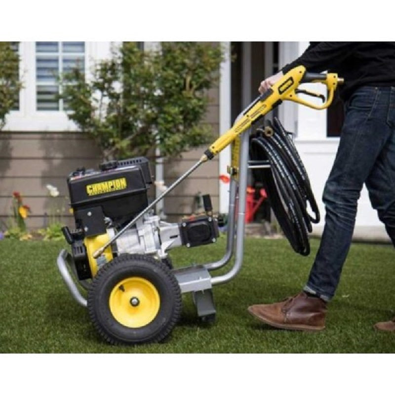 Person moving the Champion 4200PSI Pressure Cleaner across green grass near a house. The yellow and black washer with hose and spray gun is shown being wheeled on its large tires, emphasizing portability and easy maneuvering for outdoor cleaning.