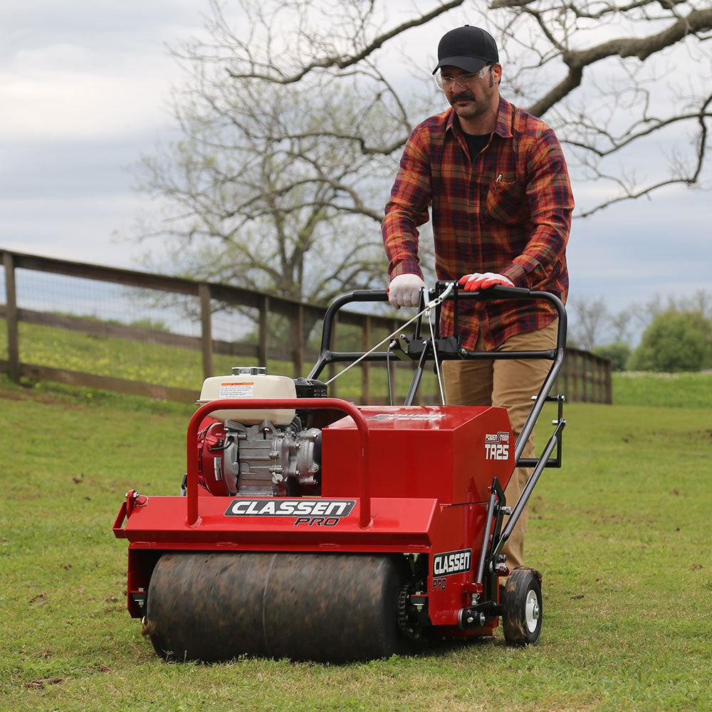 Classen TA25DA 25" PowerSteer™ PRO Aerator with Honda GX120 engine on grassy terrain, a man operating, highlighting the front drum, red Classen frame, dual handle control system, and real-time aeration during field use