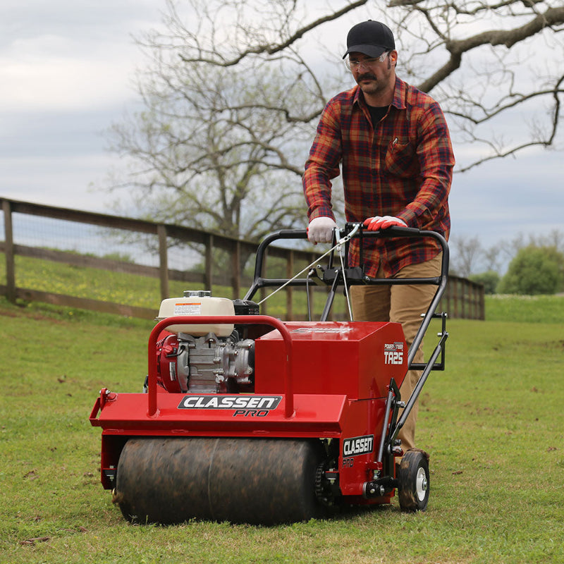 Classen TA25DA 25" PowerSteer™ PRO Aerator with Honda GX120 engine on grassy terrain, a man operating, highlighting the front drum, red Classen frame, dual handle control system, and real-time aeration during field use