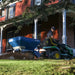EcoLawn Applicator Eco 50 spreader attached to a John Deere tractor, spreading compost evenly on a residential lawn outside a red brick house. Operator ensures professional topdressing for turf health, soil improvement, and sustainable landscape maintenance in a controlled environment.