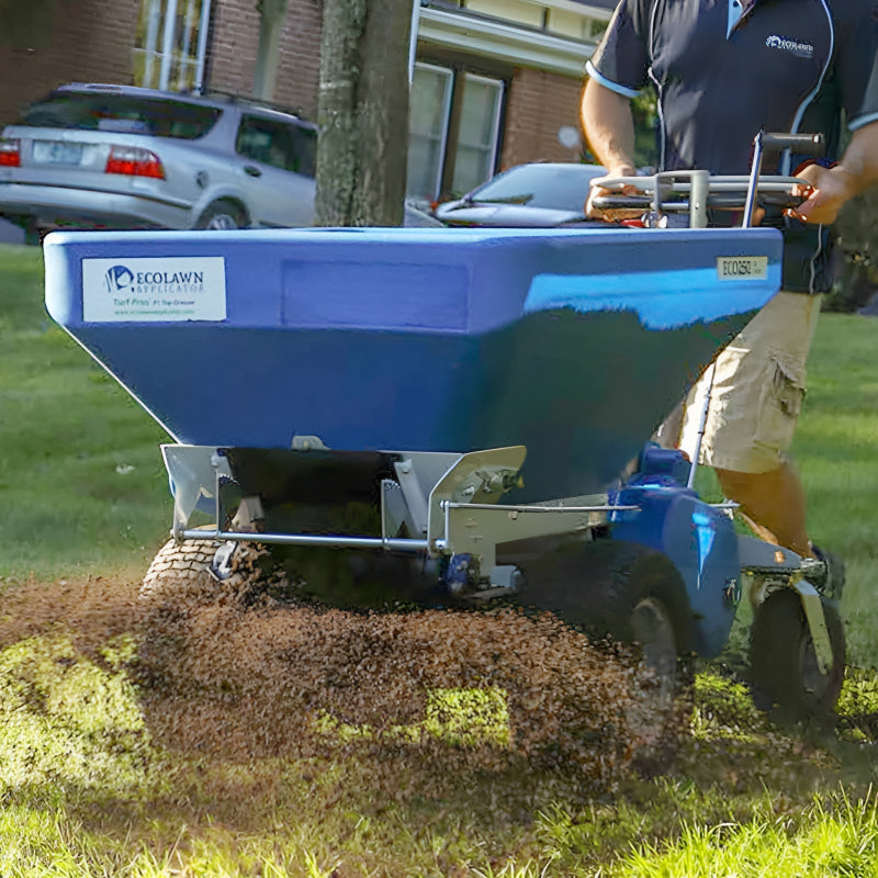 Eco 250 Top Dressing Spreader photographed from a side angle while in operation, spreading material evenly over a lawn. A person guides the machine, showcasing its efficiency and precision for turf care in residential or professional landscaping applications.