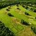 Aerial view of a large golf course showcasing the extensive mowing coverage achievable with the FJD RCM01 Robotic Lawn Mower, featuring striped fairways, greens, bunkers, and expansive commercial turf maintenance across multiple course sections.