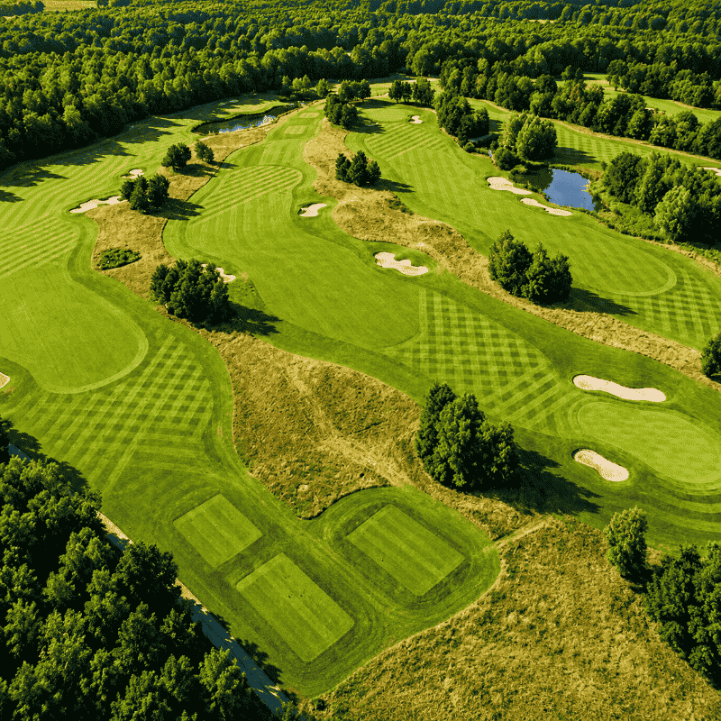 Aerial view of a large golf course showcasing the extensive mowing coverage achievable with the FJD RCM01 Robotic Lawn Mower, featuring striped fairways, greens, bunkers, and expansive commercial turf maintenance across multiple course sections.