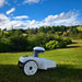 FJD FR4000 robotic lawn mower positioned on a neatly mowed grassy field with rolling hills, trees, and bright blue skies in the background. The autonomous unit stands ready for precision lawn maintenance in a peaceful, natural outdoor landscape.