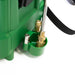 The image shows a close-up view of a green component of what appears to be a sprayer unit, specifically identified as part of a FlowZone Typhoon G3 + Swap Tank MicroBurst Pest Pack. The green component features a molded holder designed to secure a metallic spray wand, which is partially visible. Brass fittings are prominently displayed, including a valve mechanism and connection points for the wand and potentially other components of the spraying system. A black strap, likely part of a shoulder harness for 