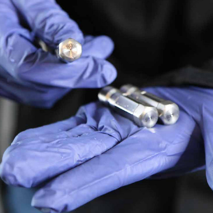 Technician wearing blue gloves holding FlowZone stainless steel spray nozzles, showcasing durable interchangeable tips for MicroBurst battery backpack sprayer.