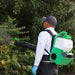 Man using FlowZone Vortex 10L Backpack Mister to spray mist onto dense green bushes for pest control and plant care.