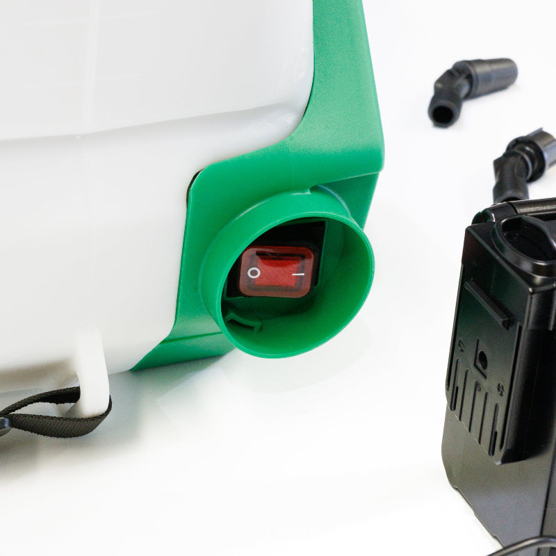 Close-up view of the FlowZone Zephyr 3 15L battery-powered sprayer showing the red on/off power switch housed in a green casing at the base of the tank. Battery pack and accessories are partially visible in the background.