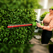 Greenworks 40V Hedge Trimmer trimming a dense garden hedge, demonstrating cordless battery-powered performance, dual-action steel blades, lightweight handling, and precise cutting for shaping shrubs, hedges, and ornamental plants in residential landscape maintenance.