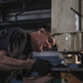 ISOtunes Free 2.0 wireless earbuds worn by a tradesperson operating industrial machinery, providing Bluetooth audio and in-ear hearing protection to reduce noise exposure while allowing communication during workshop and manufacturing tasks.