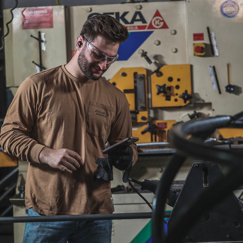 ISOtunes Free 2.0 true wireless earbuds worn by a worker in a workshop, providing Bluetooth audio and hearing protection while operating machinery, allowing hands-free calls and noise reduction in industrial environments.
