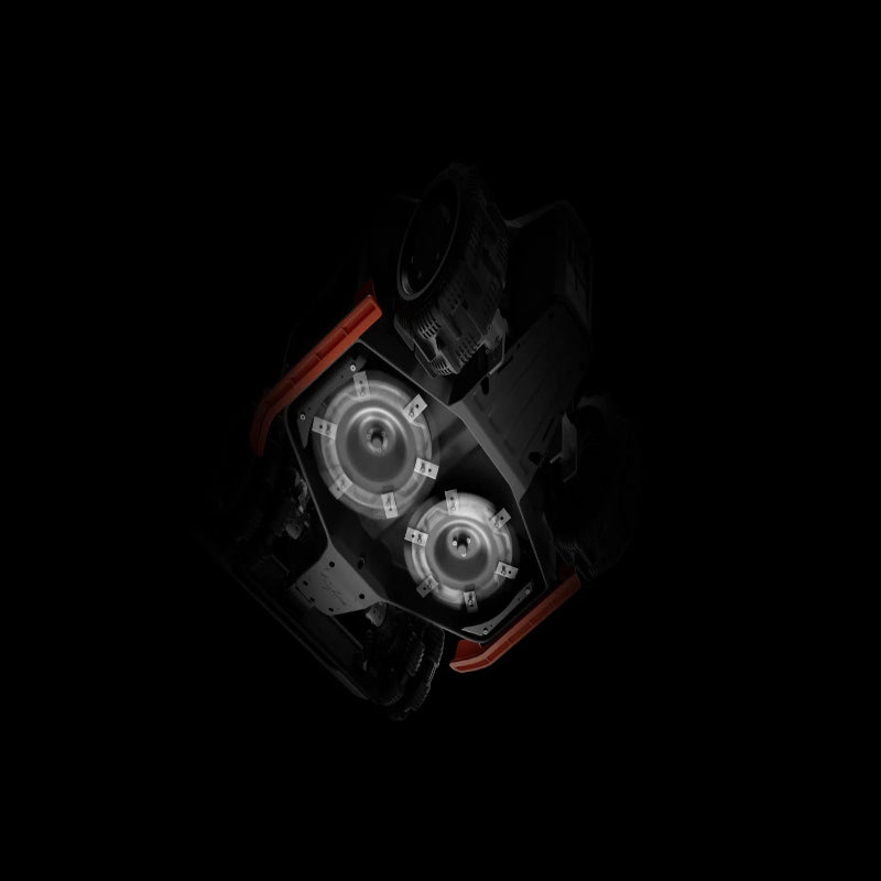 Underside view of the Mammotion Luba AWD X robotic lawn mower showing its dual spinning cutting discs with multiple sharp blades, highlighted against a dark background to emphasize the advanced mowing system and cutting width design.