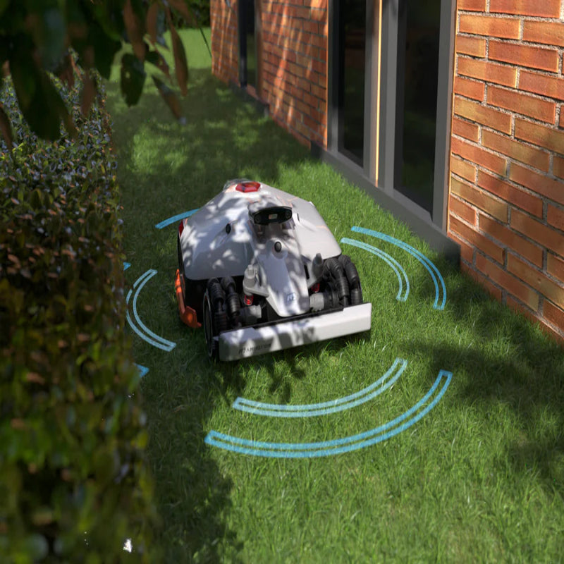Mammotion Luba AWD X robotic mower navigating grass near a hedge and brick house wall. Blue sensor waves illustrate obstacle detection technology, ensuring safe and precise mowing in tight spaces with natural sunlight casting shadows.