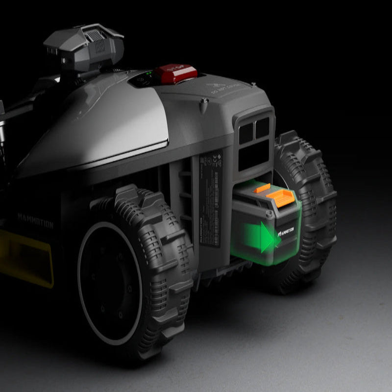 Close-up of the Mammotion Luba Mini robotic lawn mower showing its rear section with large rugged wheels and a removable black battery featuring orange latches and a glowing green arrow indicator, set against a dark background.
