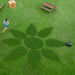A top-down view of a bright green lawn where a Mammotion YUKA Mini mower creates a flower-shaped mowing pattern, while 1 children run nearby beside a hammock, wooden bench, and small dog house.