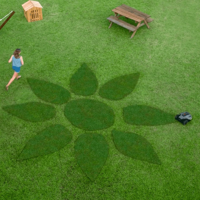 A top-down view of a bright green lawn where a Mammotion YUKA Mini mower creates a flower-shaped mowing pattern, while 1 children run nearby beside a hammock, wooden bench, and small dog house.