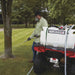 Man using NorthStar 12V ATV sprayer to water or apply herbicide around a tree, with the sprayer mounted on a red ATV and connected via a long hose for precise application.