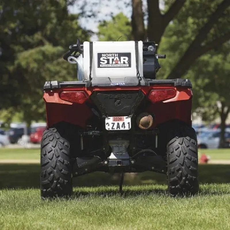 NorthStar 12V ATV sprayer mounted on a red Polaris quad bike, shown from the rear on green grass. The durable tank and hose system are ready for spraying applications in lawns, gardens, or agricultural settings.