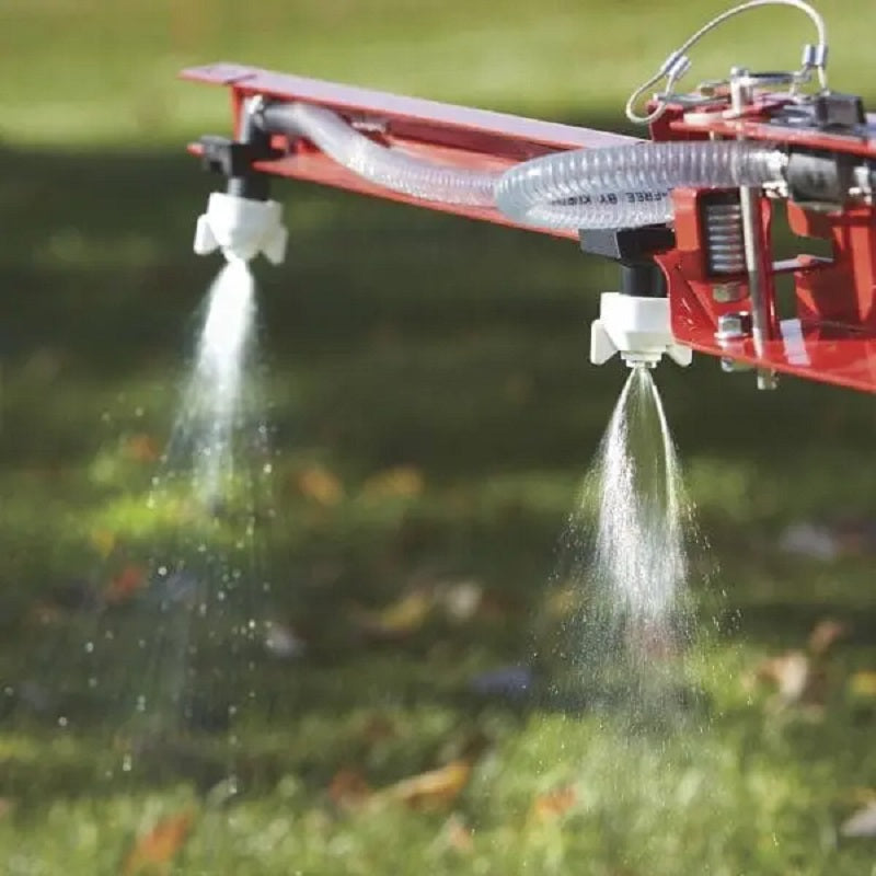Close-up of NorthStar tow-behind sprayer boom showing dual nozzles spraying fine mist over green grass. Features red metal frame, clear tubing, and even spray pattern in outdoor sunlight for precision lawn and garden treatment.