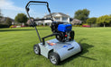 Predator LS460 lawn scarifier featuring a blue GB225 engine and silver steel housing, designed for professional lawn dethatching and aeration. Photographed on a lush green lawn with a large house and trees in the background under clear skies.