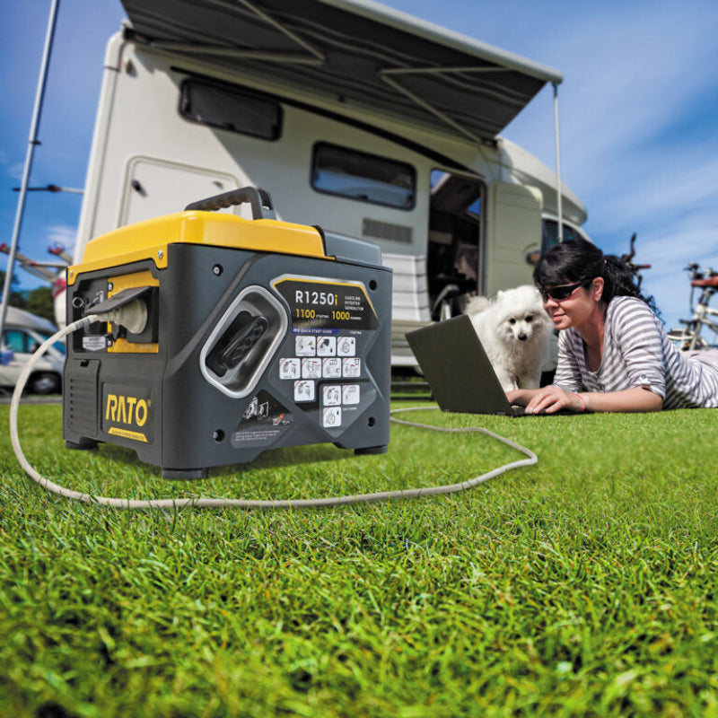 The image depicts a RATO R1250i inverter generator, a portable power source suitable for camping and outdoor activities, shown in a grassy area outside what appears to be a recreational vehicle or camper. A woman and a Japanese Spitz dog are also present, with the woman using a laptop, suggesting the generator is being used to power electronic devices in a recreational setting. 