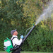 Man wearing a FlowZone Vortex 10L Backpack Mister spraying mist upward into trees in a green outdoor environment, demonstrating powerful reach and coverage for pest control and lawn care.